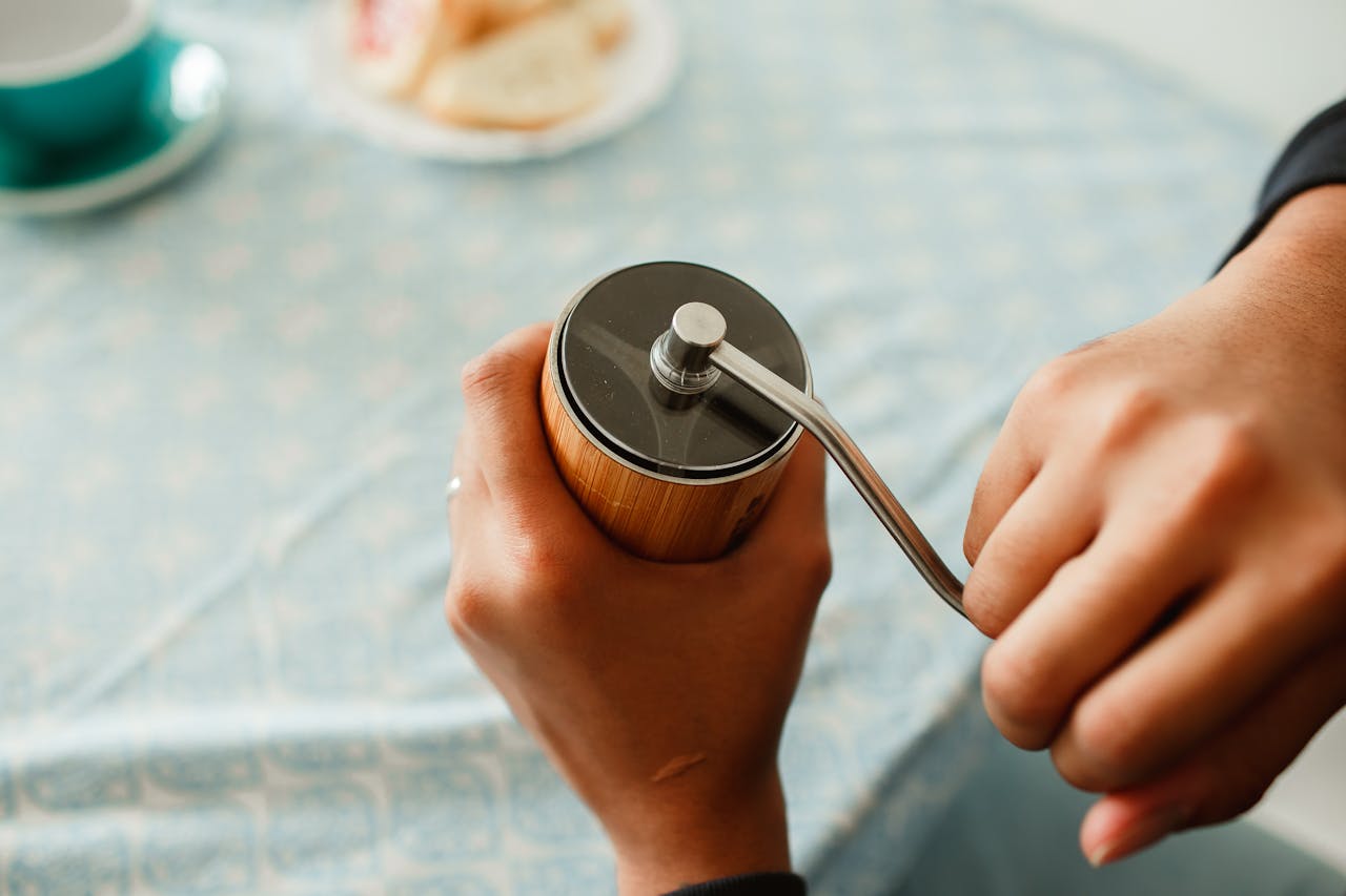 services-01 A person using a manual coffee grinder on a patterned tablecloth, preparing fresh coffee.